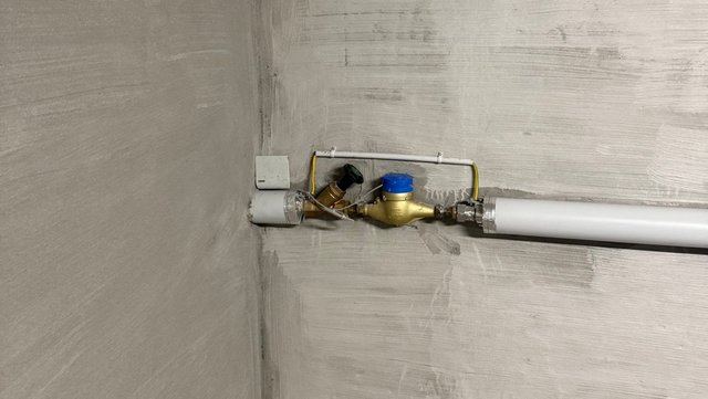 Wasserzähler an weißer Rohrleitung vor grauer Wand, Nahaufnahme