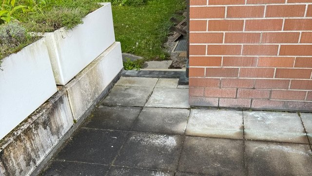 Verschmutzte Terrassenplatten neben Ziegelwand und Pflanzkübeln, Nahaufnahme