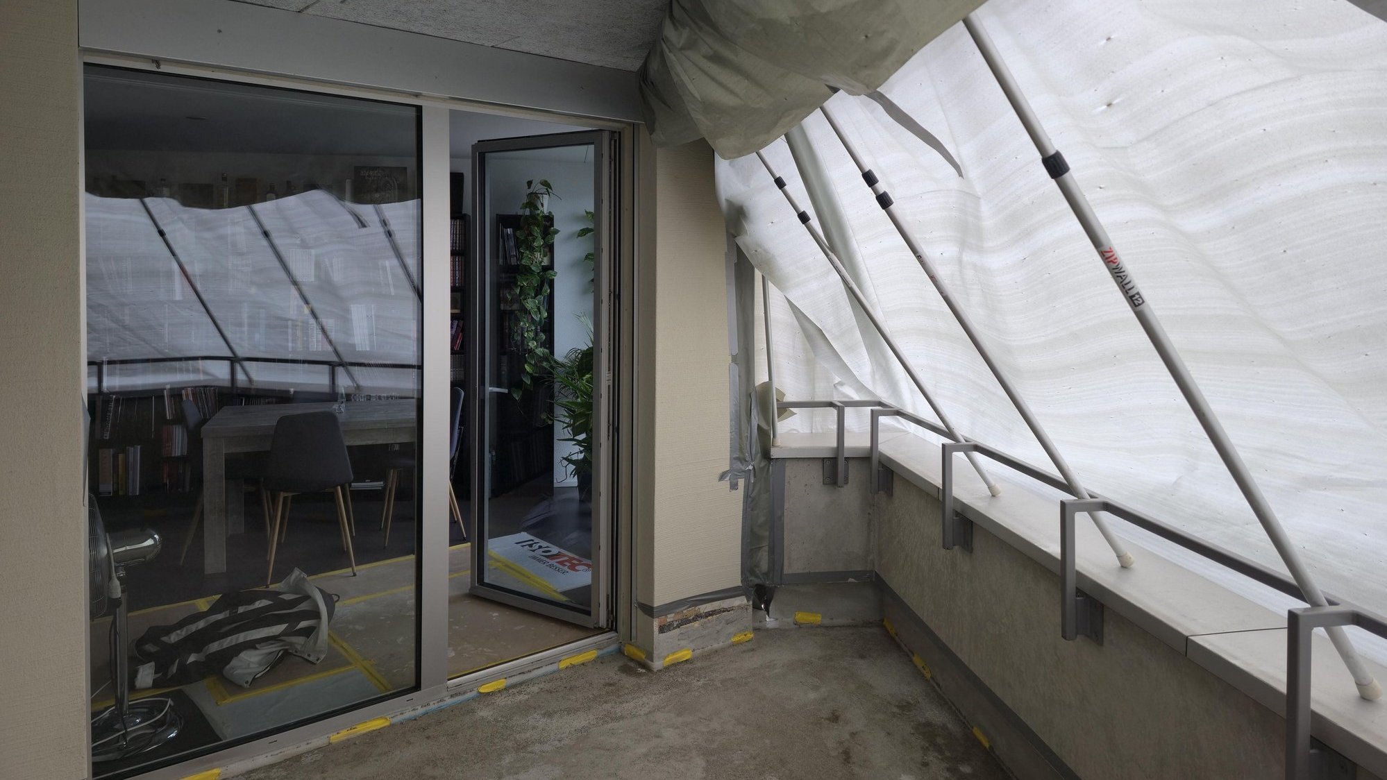 Balkon mit Schutzfolie und Stangenkonstruktion vor geoeffneter Schiebetuer