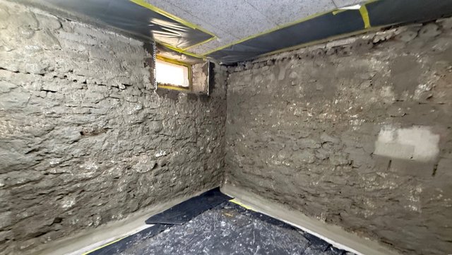 Graue Masse auf Kellerwänden, kleines Fenster und abgedeckter Boden