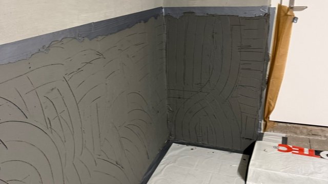 Schwarze Masse auf Wand-Ecke aufgetragen, strukturierte Spachtelspuren sichtbar