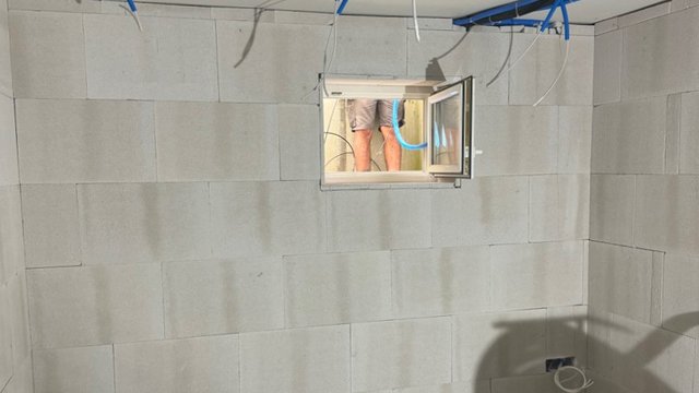 Kellerwand aus hellen Platten mit offenem Fenster und hängenden Kabeln