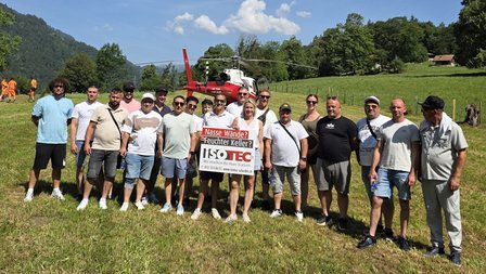 ISOTEC Teamfoto mit Werbeschild vor rotem Helikopter auf grüner Wiese