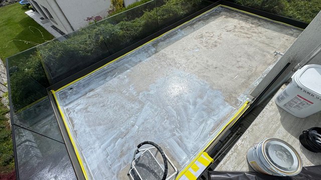 Abgeklebter Balkonboden mit hellgrauer, verschmierter Beschichtung und Eimern am Rand