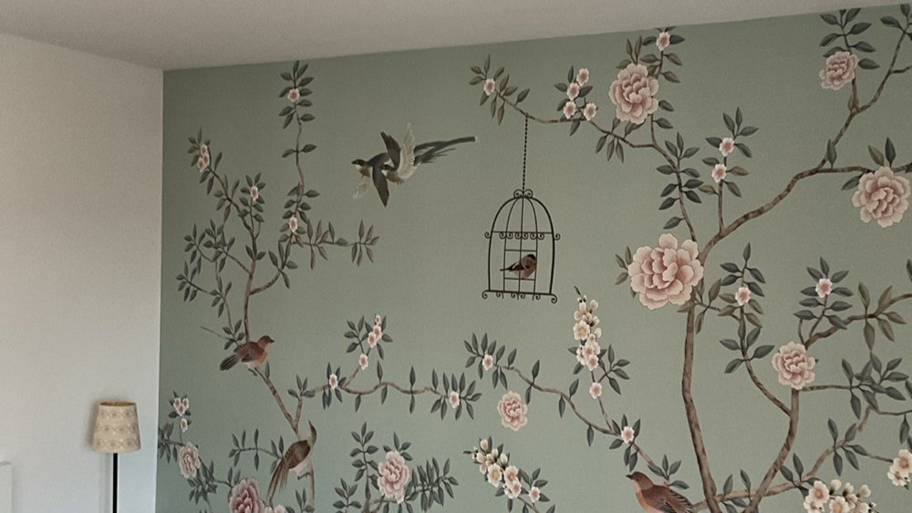 Grünliche Tapetenwand mit Blütenzweigen, Vögeln und hängendem Vogelkäfig