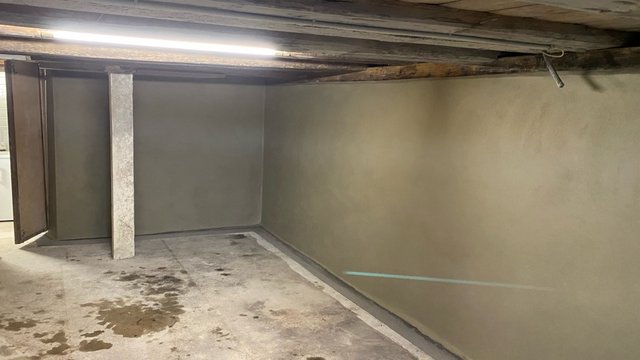 Leerer Kellerraum mit glatten beigegrauen Wandflächen und Flecken am Boden.