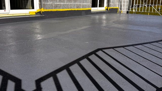 Schwarze Beschichtung auf Balkonboden vor Gebäudefassade