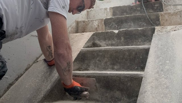 Arbeiter glättet graue Masse auf Betontreppe mit Glättkelle.