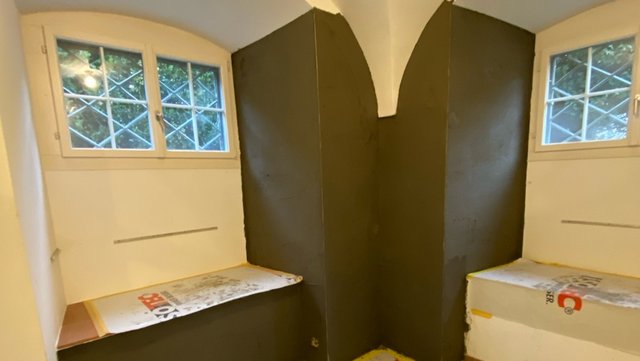 Schwarze Masse auf Kellerwänden zwischen zwei Fenstern