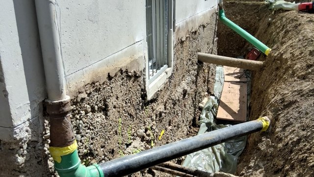 Freigelegte Hauswand im Erdgraben mit Kiesbeton und Rohrleitungen