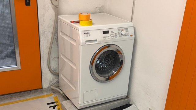 Weiße Waschmaschine steht in Raumecke vor Wand mit dunklen Flecken