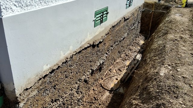 Freigelegte Gebäudewand mit grober grauer Masse im Erdgraben