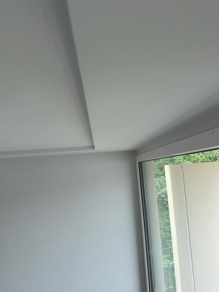 Weiße Zimmerwand mit Deckenabsatz neben Fensterfront, Innenraumansicht