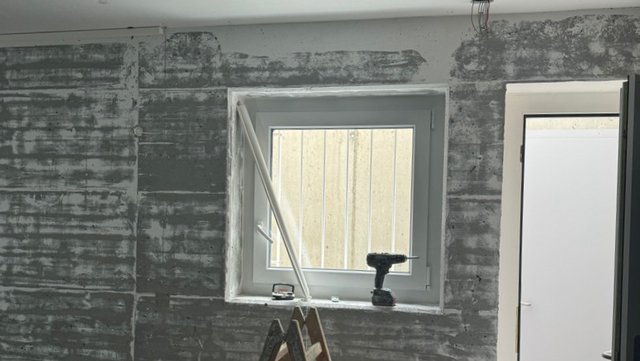 Freigelegte Wand mit Fensteröffnung und dunklen Rückständen im Raum