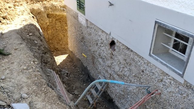 Freigelegte Kellerwand neben Baugrube mit Erdreich, Leiter und Kabelschläuchen