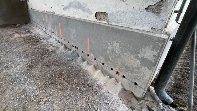 Reihe Bohrlöcher in grauer Masse am Sockelbereich einer Betonfläche, Nahaufnahme