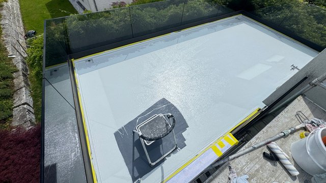Frisch beschichtete Flachdachfläche mit Abklebeband, Trittstufe und Farbeimer am Rand