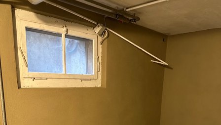 Kleines Kellerfenster mit Kondensspuren, daneben ausziehbare Wäscheleine an der Decke
