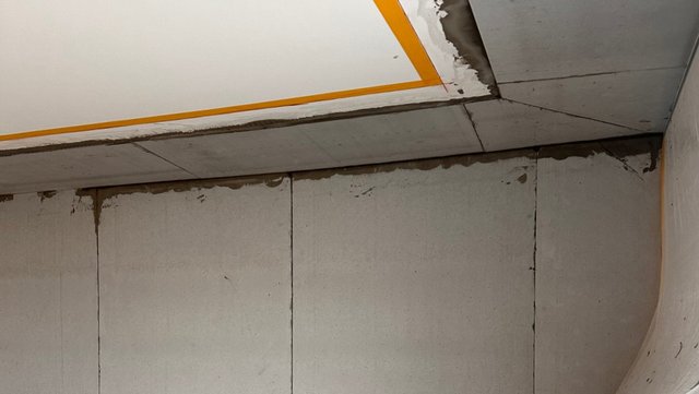 Abgehängte Decke mit verfärbten Fugen und bröckelnder Kante in Zimmerecke