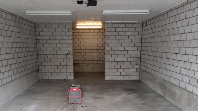 Leerer Kellerraum mit grauen Betonwänden, Ziegelmuster und rotem Trocknungsgerät am Boden
