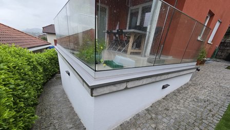 Glasgeländer-Balkon über weißer Wand mit nassem Pflasterweg