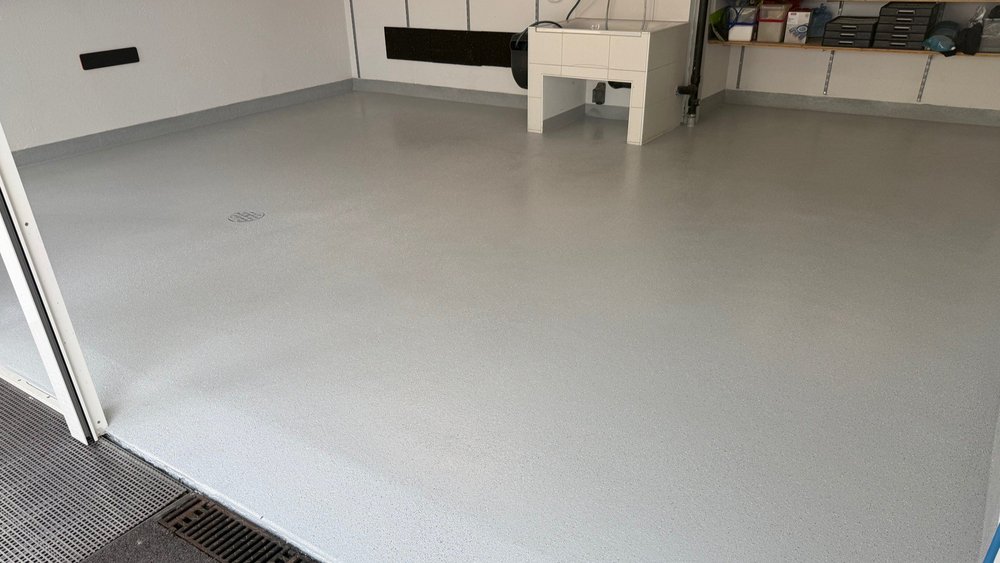Glatter grauer Bodenbelag in Werkraum mit Abfluss und gefliester Arbeitsbank