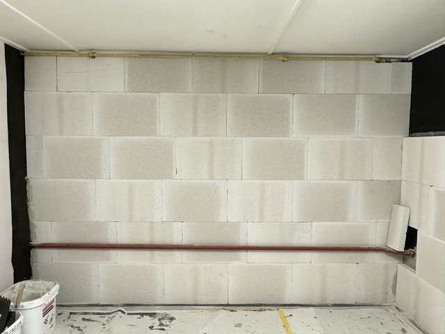 Helle Plattenverkleidung an Kellerwand, rote Leitung horizontal montiert.