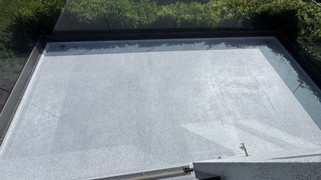 Graue Dachfläche mit Metalldetails, von oben fotografiert, Grünbewuchs am Rand