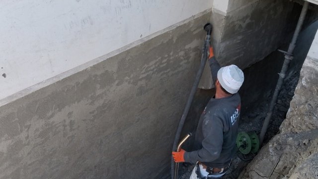 ISOTEC Mitarbeiter saugt Bohrmehl von freigelegter Hauswand im Graben ab