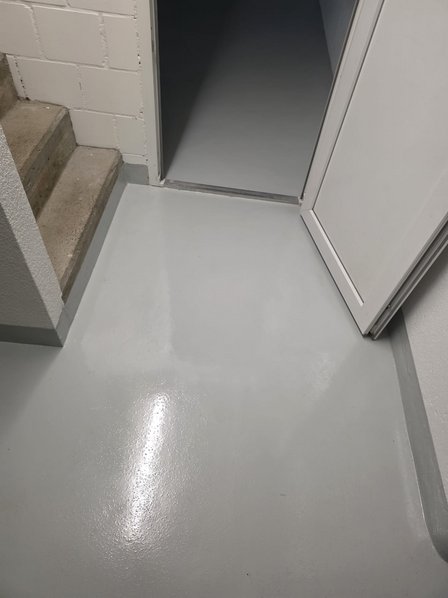 Grauer beschichteter Boden vor Treppe und offener Tür im Kellerraum