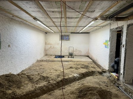Kellerraum mit freigelegtem Erdreich und Graben, isolierte Decke mit Leuchten.