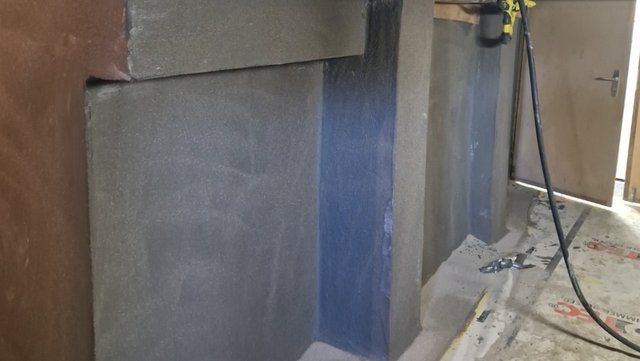 Dunkle Masse frisch auf graue Wandfläche aufgetragen, Nahaufnahme.