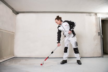 ISOTEC Mitarbeiter verteilt dunkle Flüssigkeit auf Kellerboden.