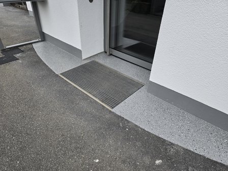 Graue Eingangsstufe mit rutschfester Matte vor Glastuer