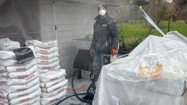 ISOTEC Mitarbeiter steht neben Sackstapeln und Maschine unter Zeltdach, Außenbereich