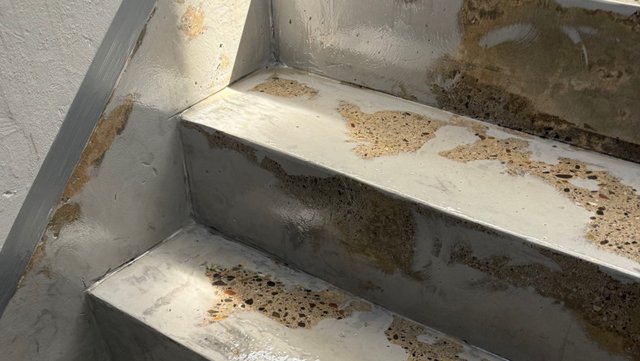 Beschädigte Treppenstufen mit abgeplatzter grauer Beschichtung und freiliegendem Beton.