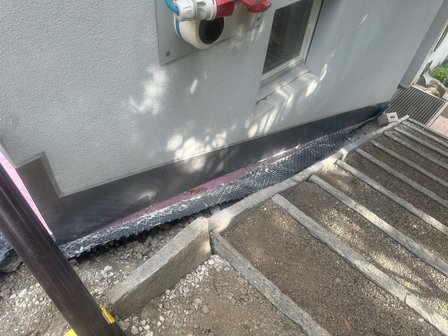 Schwarze Noppenbahn entlang Gebäudewand neben Erdweg