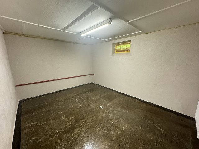 Leerer Kellerraum mit weiß gestrichenen Wänden, Betonboden und kleinem Fenster