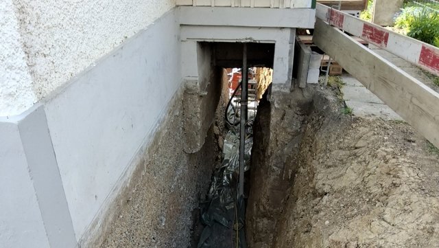Freigelegte Kellerwand in schmalem Erdgraben an Gebäude