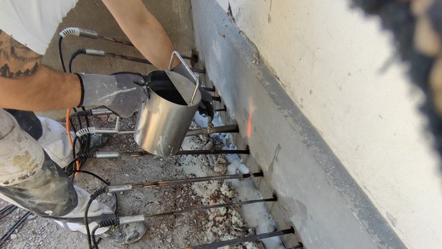 Arbeiter injiziert schwarze Masse mit Metallbehälter in Bohrlöcher am Wandfuß.