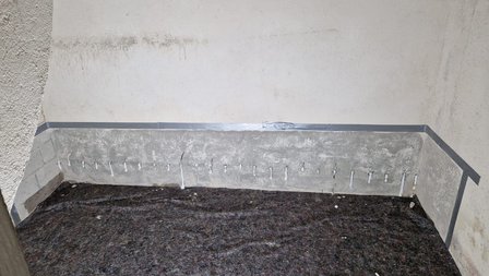 Graue Sockelzone mit Bohrlöchern und weißer Masse an Wand, Nahaufnahme