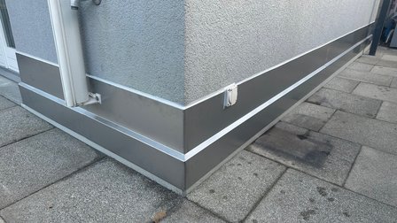 Graue Metallverkleidung am Gebäudesockel mit senkrechtem Rohr