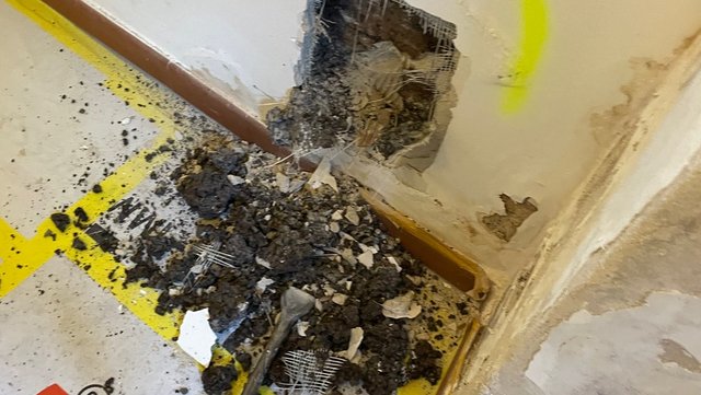 Beschädigte Wand mit freigelegtem Mauerwerk und Schutt auf dem Boden