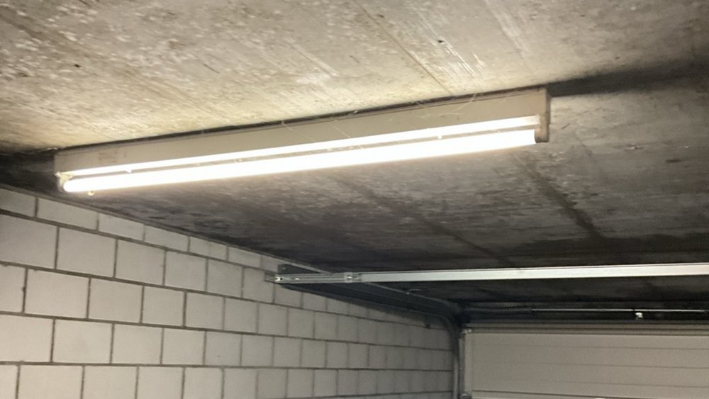 Deckenleuchte in Garage, Beton­decke mit dunkler Verfärbung über Mauerwerk.