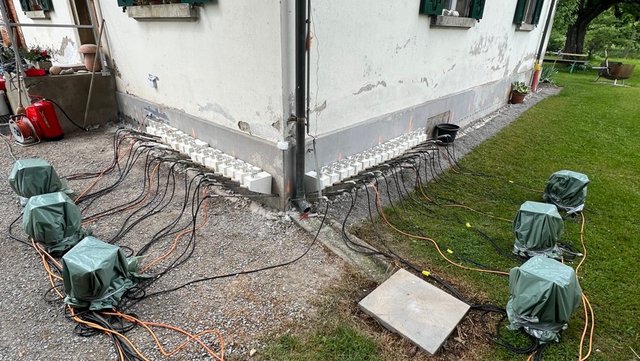 Kabel und abgedeckte Geräte an Hausfassade mit Bohrpunkten entlang Sockelzone