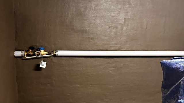 Weiße Rohrleitung mit Ventil und Messgerät vor dunkel beschichteter Kellerwand