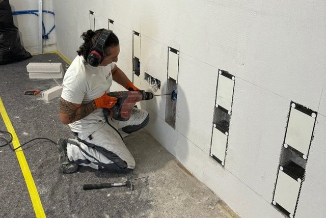 Arbeiter bohrt Löcher in helle Platte an Kellerwand