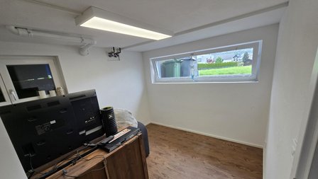 Heller Raum mit Holzfußboden, TV auf Schrank und schmalem Fenster.