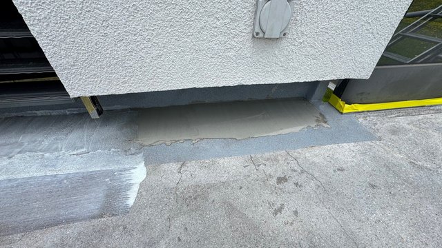 Graue Masse auf Fensterbank vor rauer Fassade, Abklebung am Rahmen