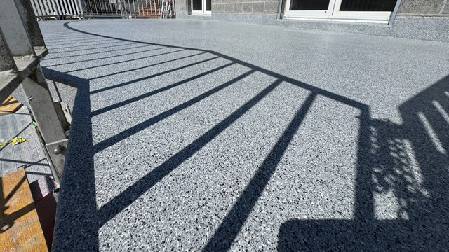 Grauer Balkonboden mit gesprenkelter Beschichtung und Geländerschatten